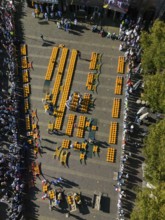 Aerial view of a busy market square with lots of cheese wheels and people at a sunny festival,