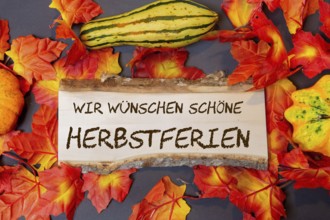(photomontage) : Wooden sign with the inscription WIR WÜSCHEN SCHÖNE HERBSTFERIEN and autumnal