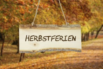 (photomontage) : Wooden sign with the inscription HERBSTFERIEN in front of an autumn-coloured