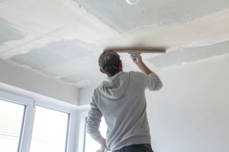 Plasterer levelling and smoothing the ceiling in the interior