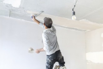 Plasterer levelling and smoothing the ceiling in the interior