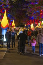 People at a colourful city festival at night with illuminated trees and stalls, Sindelfingen,