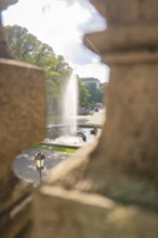 A fountain spouts water through an opening in a wall in a sunny park, Munich, Germany