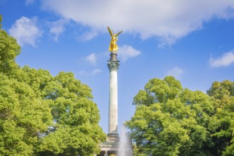 A golden statue rises on a column surrounded by trees, Munich, Germany