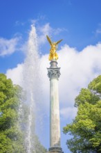 Golden statue on column with fountain and trees in front of blue sky, Munich, Germany
