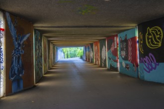 A graffiti-covered tunnel leads to a green open-air area, Munich, Germany