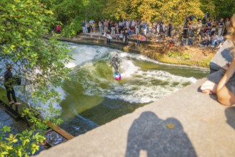 Surfer on a wave in a river, surrounded by a crowd and trees, Munich, Germany