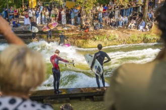 People watching surfers on an artificial wave in a river, surrounded by trees, Munich, Germany