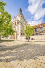 Mesmerising building surrounded by spring trees under a blue sky and paved area, Munich, Germany