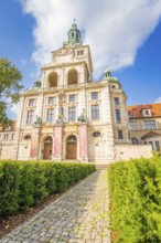 Imposing building with towers, green roofs and a cobbled path surrounded by a garden, Munich,