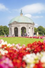 Flowery pavilion with green dome in front of a colourful flower bed and under a blue sky, Munich,