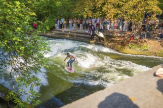 Surfers riding a powerful river wave, watched by a crowd on the shore, Munich, Germany