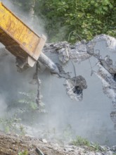 Close-up of a demolition hammer smashing concrete, surrounded by dust and plants, bridge