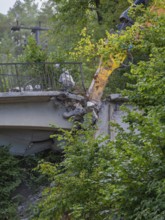 An excavator working on the end of a bridge, surrounded by dense greenery, bridge demolition, Calw,