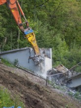 An excavator smashes concrete, dust rises, railings come loose, bridge demolition, Calw, Germany