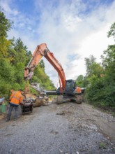 A worker and an excavator carry out work on a road covered with gravel, bridge demolition, Calw,