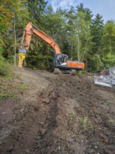 An excavator working on a pile of earth in a wooded area with a clear sky, bridge demolition, Calw,
