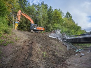 An excavator works on a demolished bridge in a wooded area, bridge demolition, Calw, Germany
