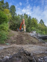 An excavator lifts earth on a slope in a forest under a blue sky, bridge demolition, Calw, Germany