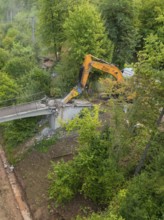 An excavator works on the demolition of a bridge from above in a forest area, bridge demolition,