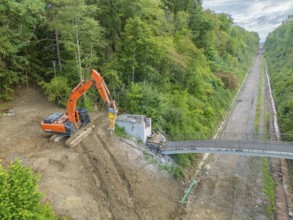 An excavator demolishes a bridge next to railway tracks in the forest, bridge demolition, Calw,