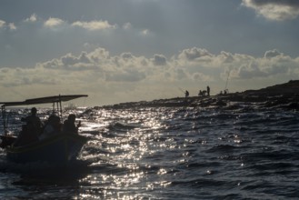 Fishermen on the coast and boat with tourists next to Marsaxlokk, southern part of Malta