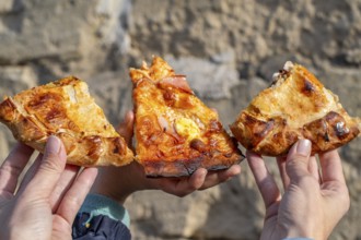 Three slices of maltese pizza hold in the hands of mother and son with stone background, Gozo,