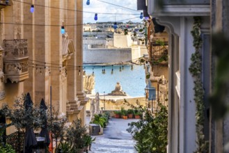 Charming downhill street illuminated with colorful bulbs in Valletta, Malta. St Angelo Fortress in