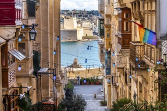 Charming downhill street illuminated with colorful bulbs in Valletta, Malta. St Angelo Fortress in
