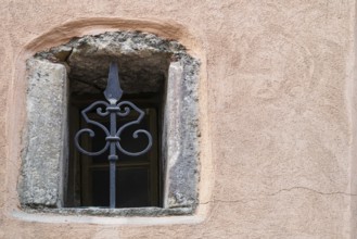 Small window with grille in an old building with pink-coloured plaster, Alsace, France
