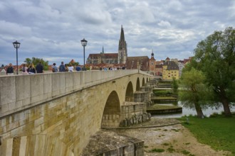 People walking across a historic bridge with a view of the cathedral and trees, Stone Bridge,