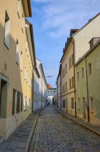 Narrow alley with cobblestones lined with colourful houses under a clear sky, Waffnergasse,