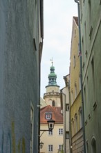 View through a narrow alley to a church tower with surrounding houses, Regensburg, Bavaria, Germany
