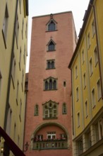High tower with ornate windows between tall, narrow buildings, Regensburg, Bavaria, Germany