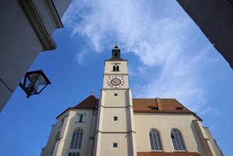 View of a high church tower with a clock under a bright blue sky, flanked by buildings,