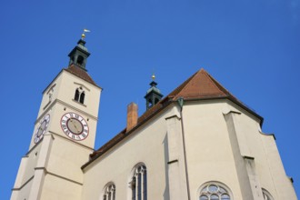 Close-up of a church tower with clock and red tiled roofs against a deep blue sky, Neupfarrkirche,