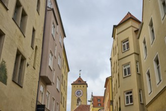 View of a tower through narrow alleys of historic buildings under a grey sky, Regensburg, Bavaria,