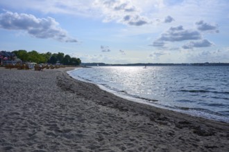 Quiet, sun-drenched beach with reflecting water and blue sky with white clouds, Heikendorf, Plön