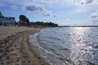 Sandy beach beach with undulating sea under a blue sky, the sun reflected on the water, Heikendorf,