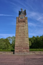 Massive memorial with eagle at the top, surrounded by trees, under a clear blue sky. Means strength