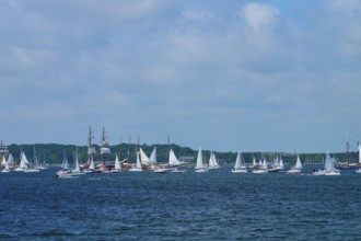 Numerous sailing boats and a large sailing ship on the open sea with a coastal view, Windjammer