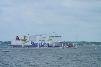Large Stena Line ferry on the sea, surrounded by smaller sailing boats under a cloudy sky,