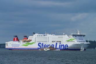 Large Stena Line ferry on the sea, accompanied by smaller sailing boats under a cloudy sky,