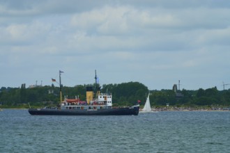 Historic icebreaker Stettin and a small sailing boat in front of a green coastal landscape and