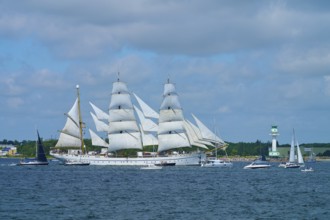 Large sailing ship Gorch Fock with white sails on the sea under a blue sky near a harbour,