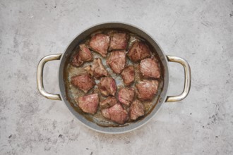 Chunks of beef are sizzling in a frying pan, showcasing a delicious golden-brown crust in the