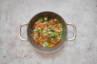 Chopped carrots, celery, and onion are frying in a pot, creating a vibrant vegetable base mixture