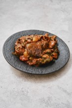 A hearty meat stew is presented on an elegant black plate. The dish features tender chunks of beef