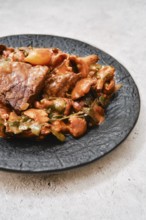 A flavorful combination of tender meat and a medley of vegetables on a black plate. The dish