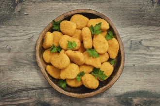 A generous serving of golden chicken nuggets is arranged in a rustic wooden bowl, garnished with